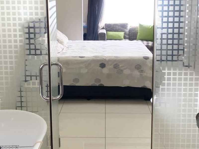A view from a bathroom with a bathtub through a frosted glass door into a bedroom with tiled flooring.