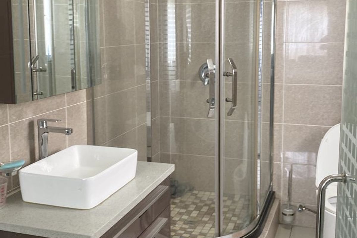 Modern bathroom featuring a curved glass shower enclosure, vessel sink on a vanity cabinet, and neutral wall tiling.