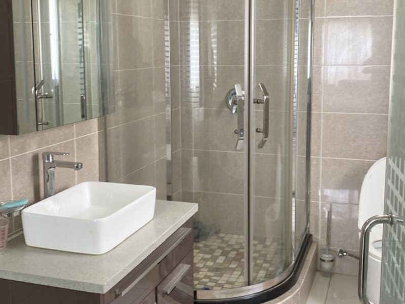 Modern bathroom featuring a curved glass shower enclosure, vessel sink on a vanity cabinet, and neutral wall tiling.