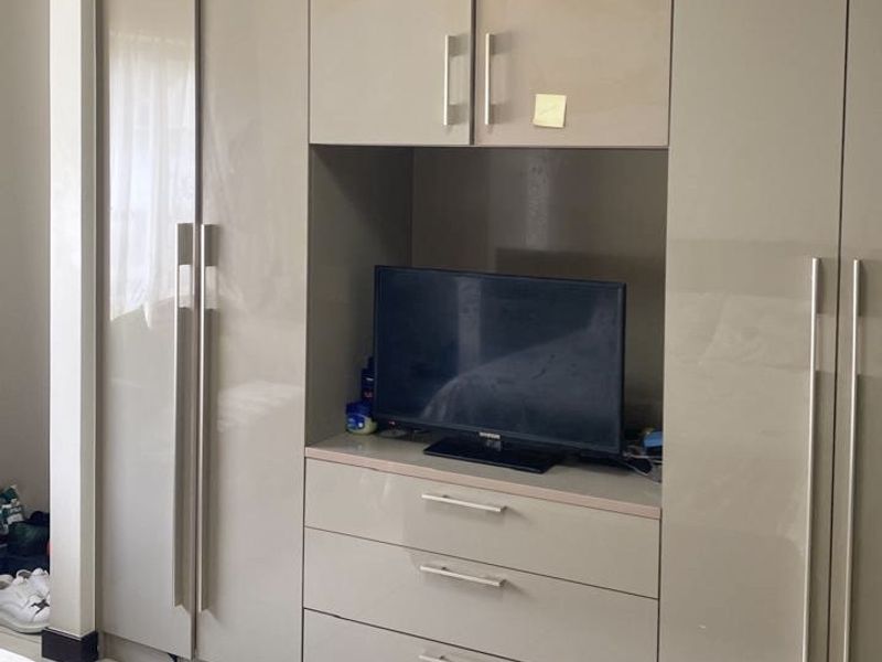 A bedroom featuring modern, high-gloss built-in cupboards with integrated storage and tiled flooring.