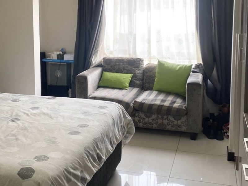 A bedroom featuring tiled flooring, built-in cupboards, and a window with curtains, providing a functional living space.
