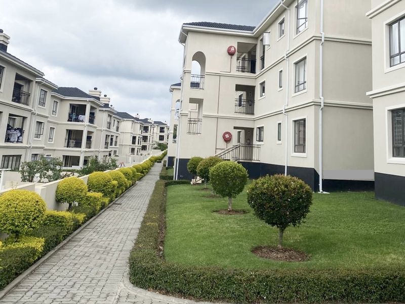 Exterior view of a multi-story apartment complex featuring well-maintained landscaped gardens, paved walkways, and building facades with balconies.