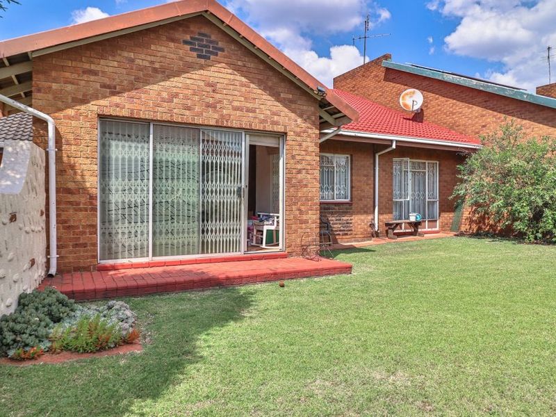 Rear view of a brick apartment featuring a private garden, tiled roof, and sliding glass doors leading to a small patio area.