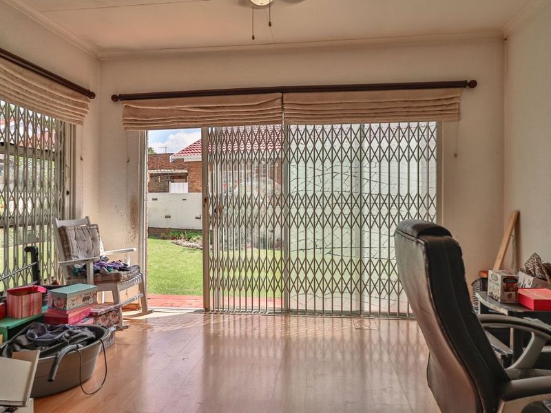 A living room featuring laminate flooring and sliding glass doors with security gates, providing direct access to the rear garden area.