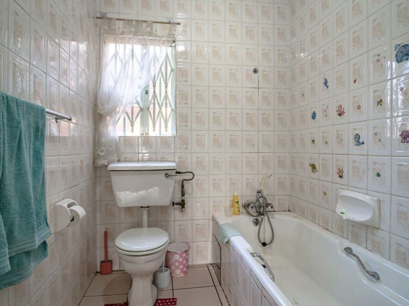A dated bathroom featuring full-height ceramic wall tiling, a standard bathtub with mixer tap, and a toilet, requiring modernization to improve aesthetic appeal.