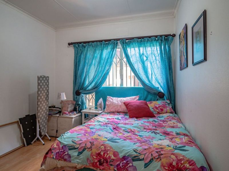 A standard bedroom featuring laminate flooring and a window fitted with a security gate, providing a functional and private sleeping space.