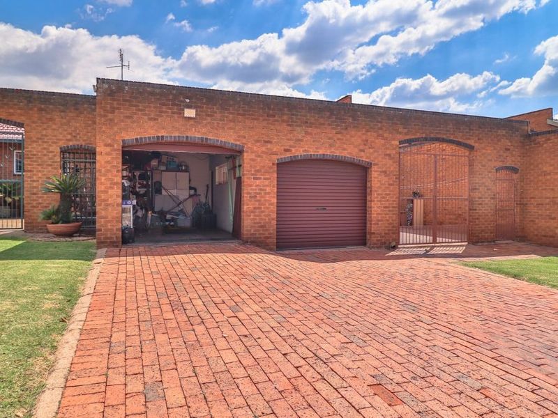 Exterior view of a brick apartment garage featuring a roller door, paved driveway, and secure metal gate access.