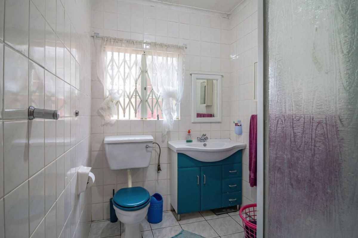 A functional bathroom featuring white wall tiles, a vanity cabinet with integrated basin, and a toilet, with a security gate on the window.