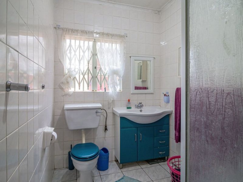 A functional bathroom featuring white wall tiles, a vanity cabinet with integrated basin, and a toilet, with a security gate on the window.