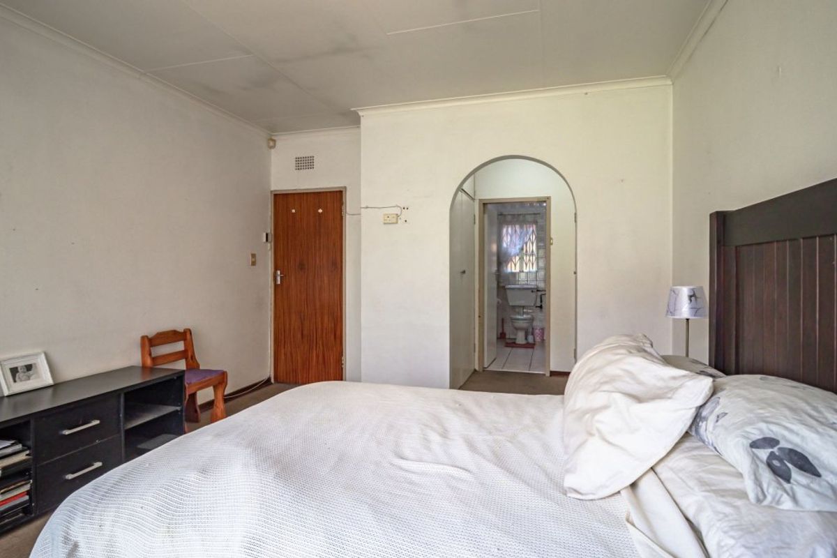 A bedroom featuring an arched doorway leading to an en-suite bathroom, with visible wear on walls and ceiling requiring cosmetic attention.