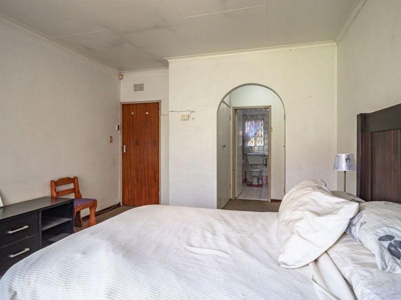 A bedroom featuring an arched doorway leading to an en-suite bathroom, with visible wear on walls and ceiling requiring cosmetic attention.