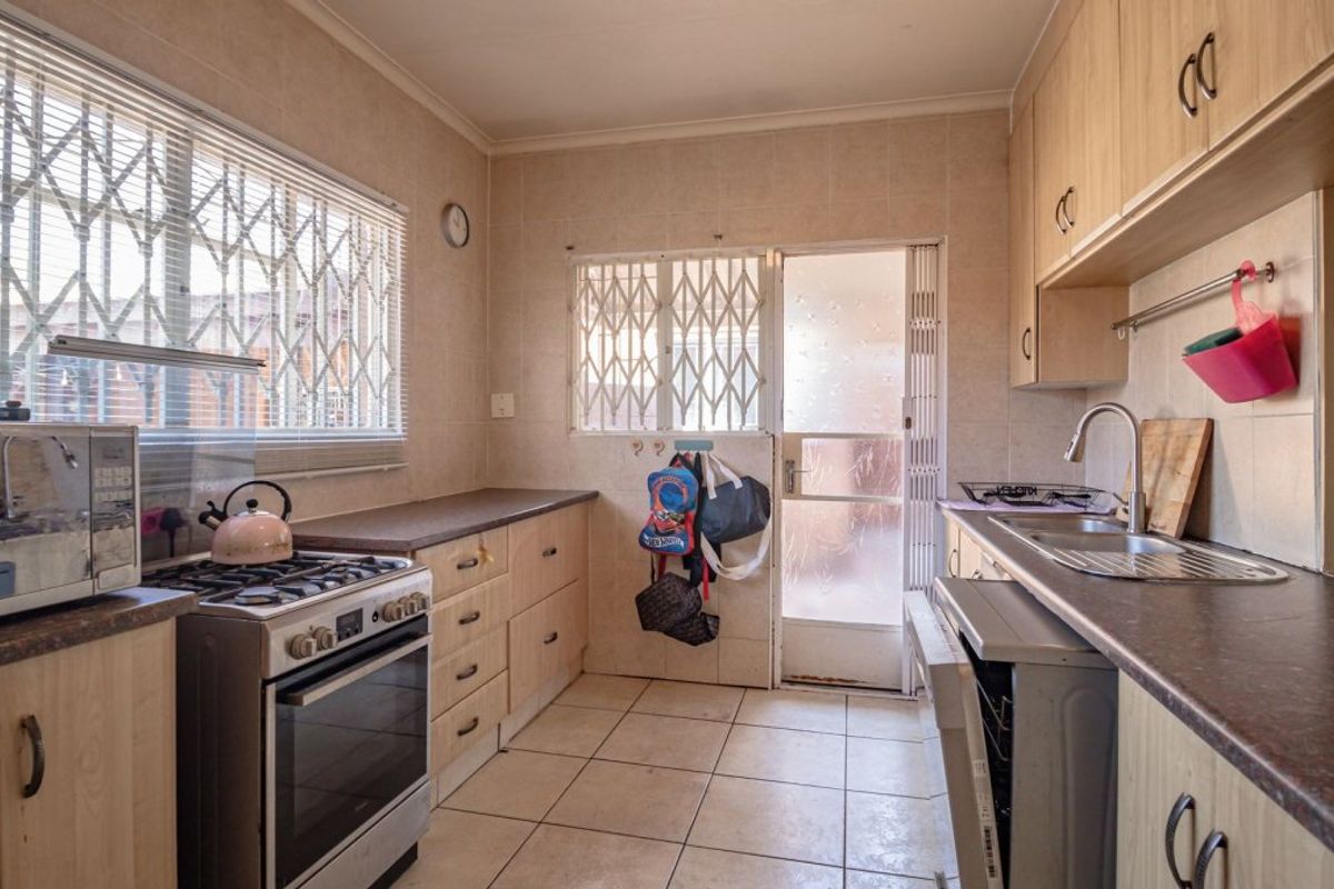 A functional kitchen featuring laminate cabinetry, a gas stove, tiled flooring, and direct access to an outdoor area through a security-gated door.