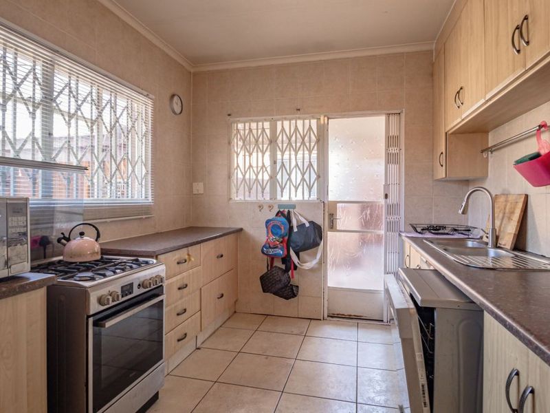 A functional kitchen featuring laminate cabinetry, a gas stove, tiled flooring, and direct access to an outdoor area through a security-gated door.