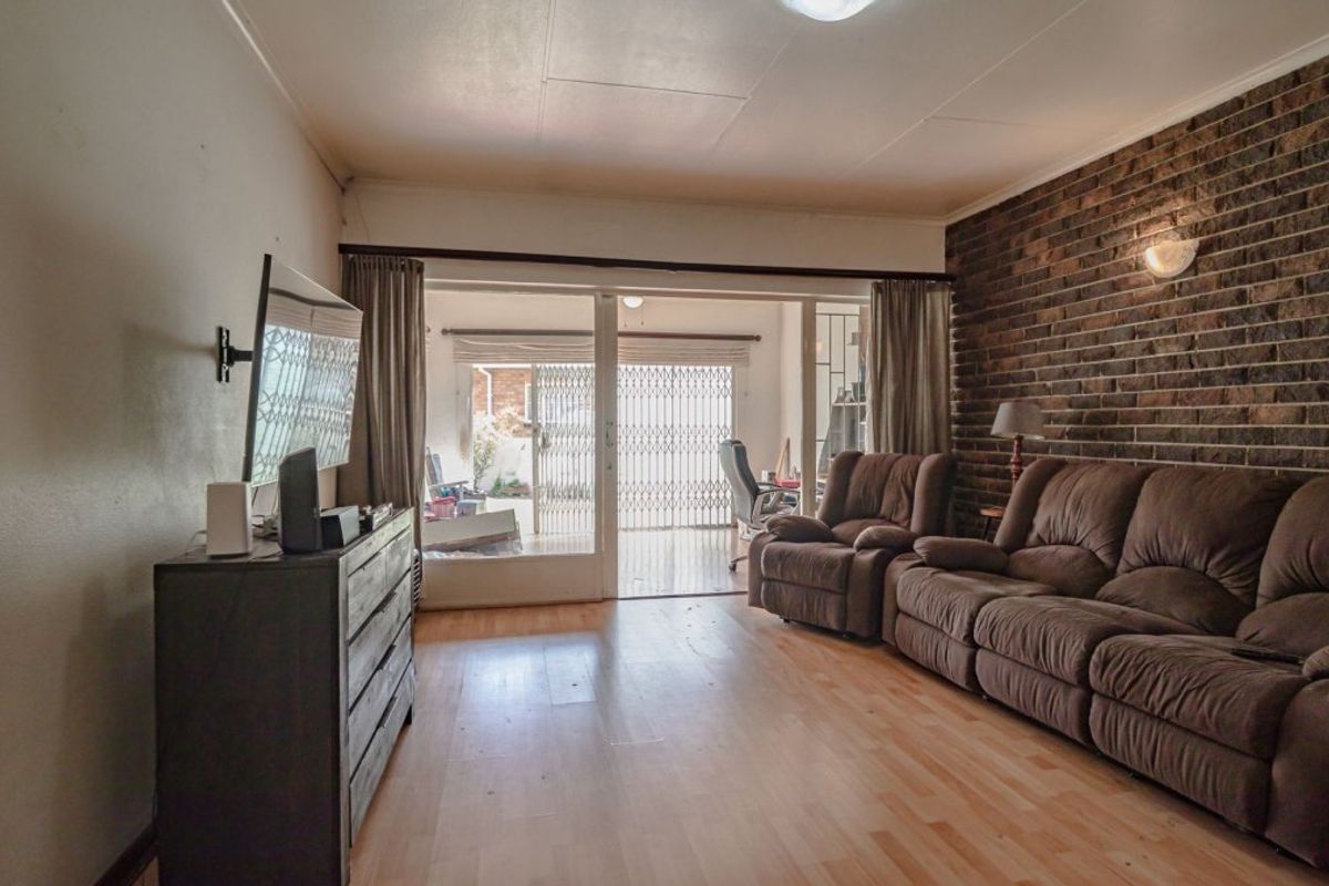 Spacious living room featuring an exposed brick accent wall, laminate flooring, and large sliding glass doors providing access to the patio area.