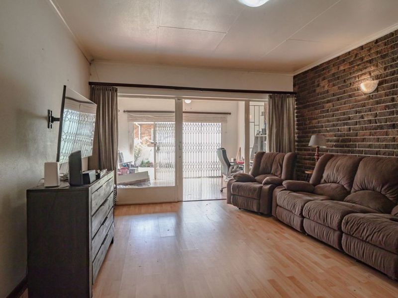 Spacious living room featuring an exposed brick accent wall, laminate flooring, and large sliding glass doors providing access to the patio area.