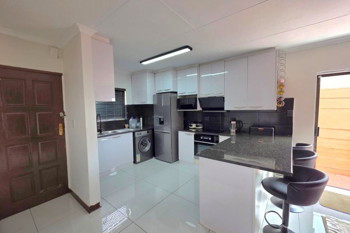 Modern kitchen featuring white cabinetry, granite countertops, a breakfast bar, built-in oven, hob, and extractor fan with tiled flooring throughout.