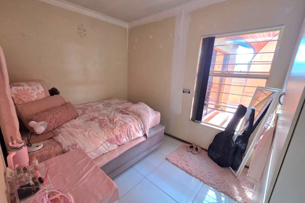 A compact bedroom featuring tiled flooring, a window with security bars, and neutral wall finishes requiring cosmetic attention.