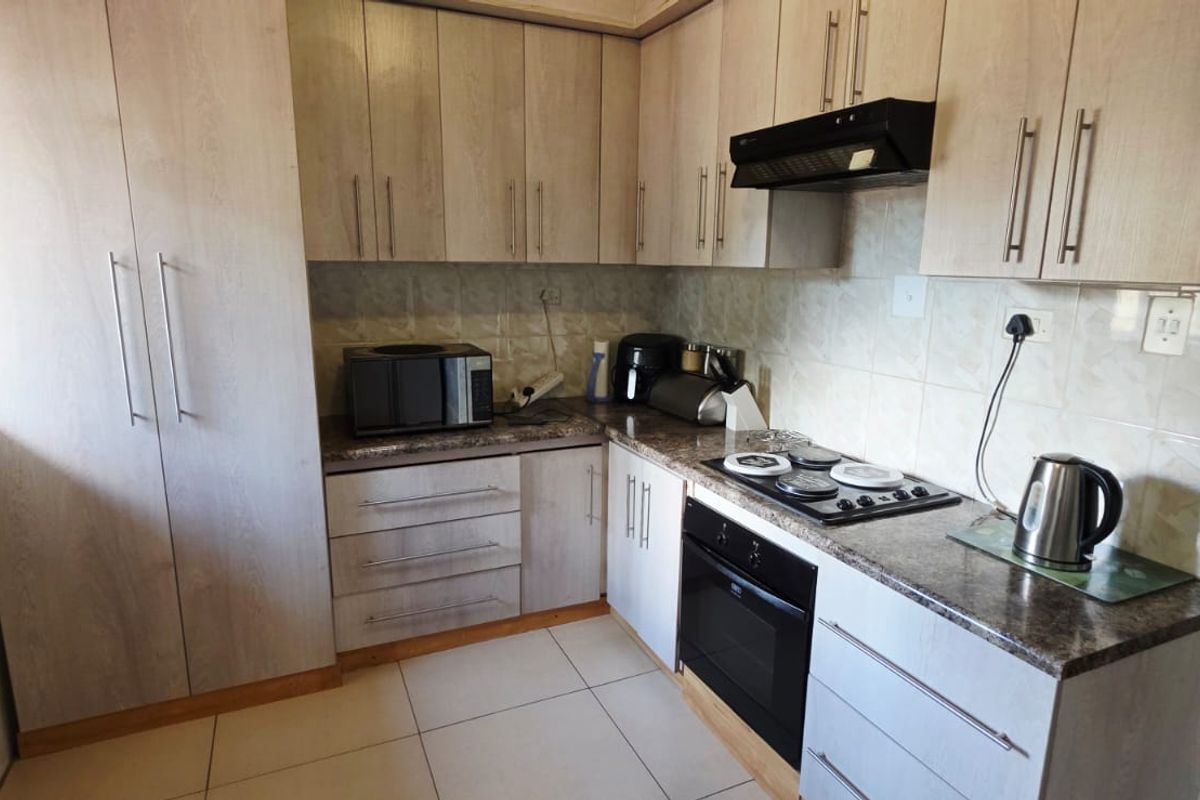 A functional kitchen featuring light wood-finish cabinetry, granite-look laminate countertops, a built-in oven, electric hob, and tiled finishes throughout.