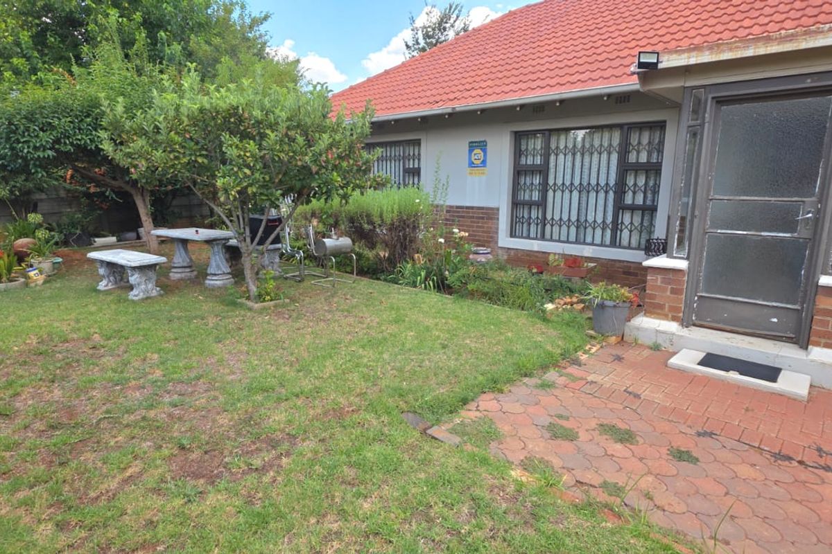 Rear garden area featuring a brick paved patio, lawn, and exterior facade with security gates and tiled roof.