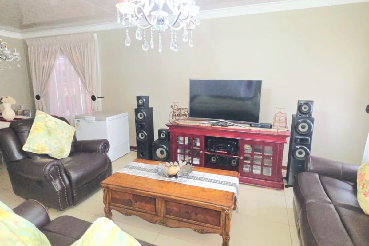 A spacious living room featuring tiled flooring, decorative ceiling coving, and a crystal chandelier, providing a comfortable and well-lit area for relaxation.