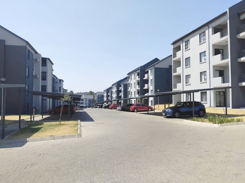 A view of the apartment complex exterior featuring paved driveways, covered parking bays, and multi-story residential buildings with balconies.