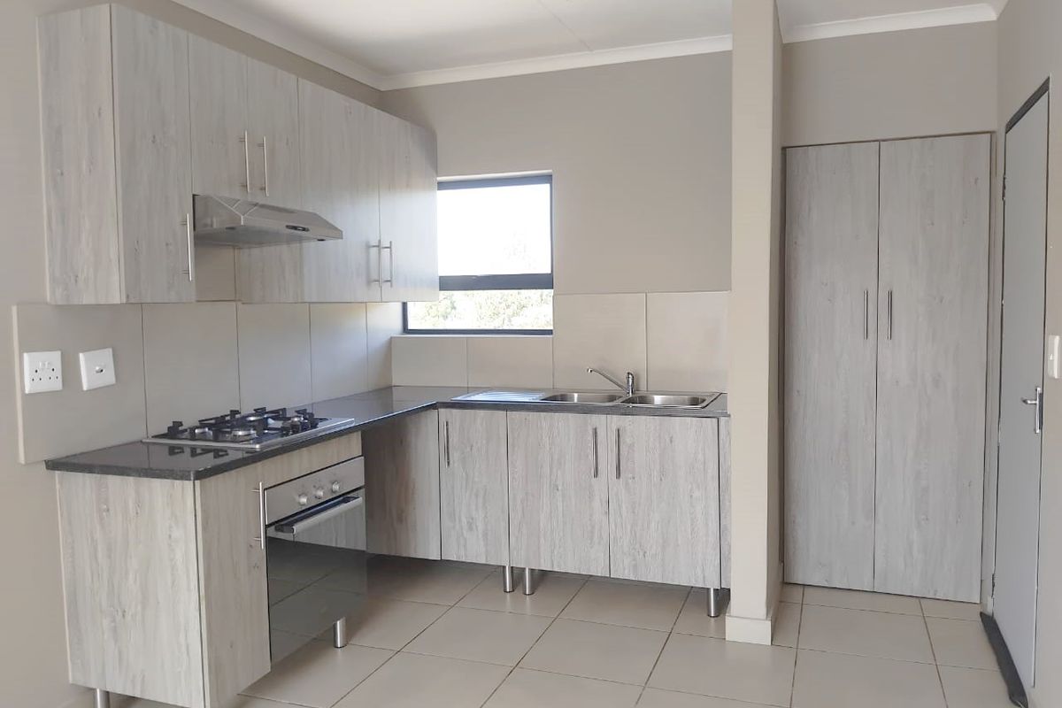 Modern kitchen featuring light wood-grain cabinetry, gas hob, electric oven, extractor fan, double sink, and tiled flooring in a clean, neutral space.