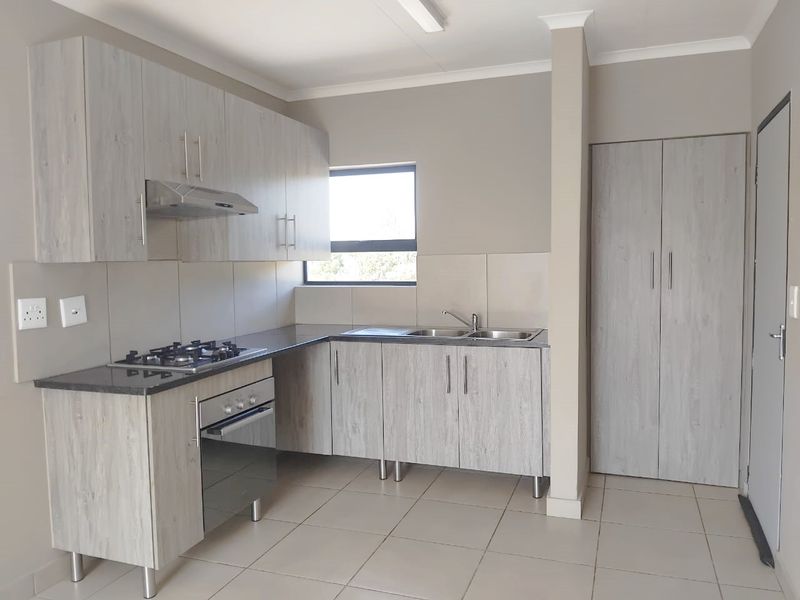 Modern kitchen featuring light wood-grain cabinetry, gas hob, electric oven, extractor fan, double sink, and tiled flooring in a clean, neutral space.