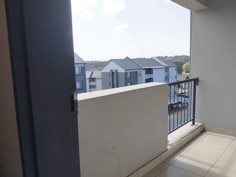A covered balcony featuring tiled flooring and a metal balustrade, offering an elevated view of the surrounding apartment complex.