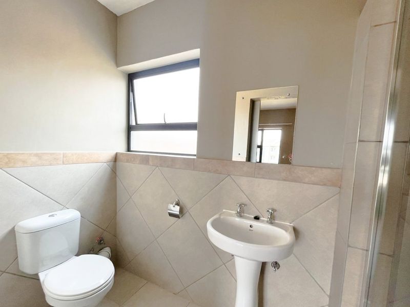 A functional bathroom featuring a pedestal basin, toilet, and neutral tiled finishes with a top-hung window for natural light.