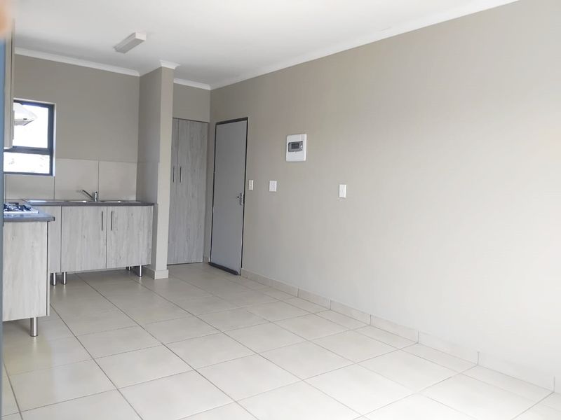 An open-plan living and kitchen area featuring neutral wall tones, tiled flooring, built-in cabinetry, and a functional kitchen layout.