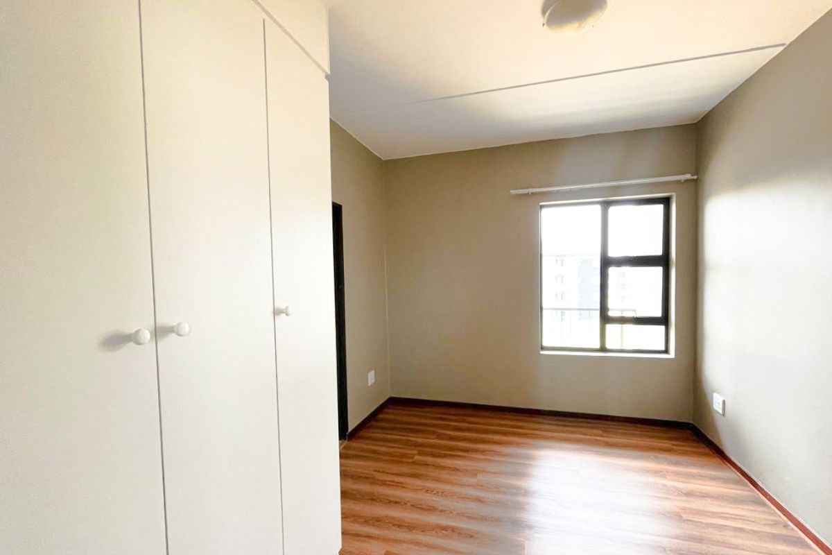 A bright, empty bedroom featuring laminate flooring, neutral wall tones, and built-in cupboards, offering a clean and versatile space.