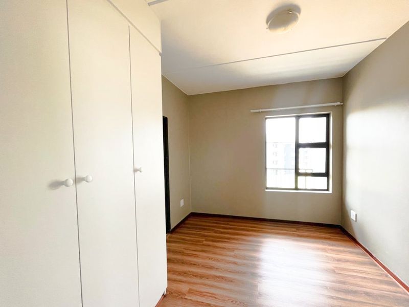 A bright, empty bedroom featuring laminate flooring, neutral wall tones, and built-in cupboards, offering a clean and versatile space.