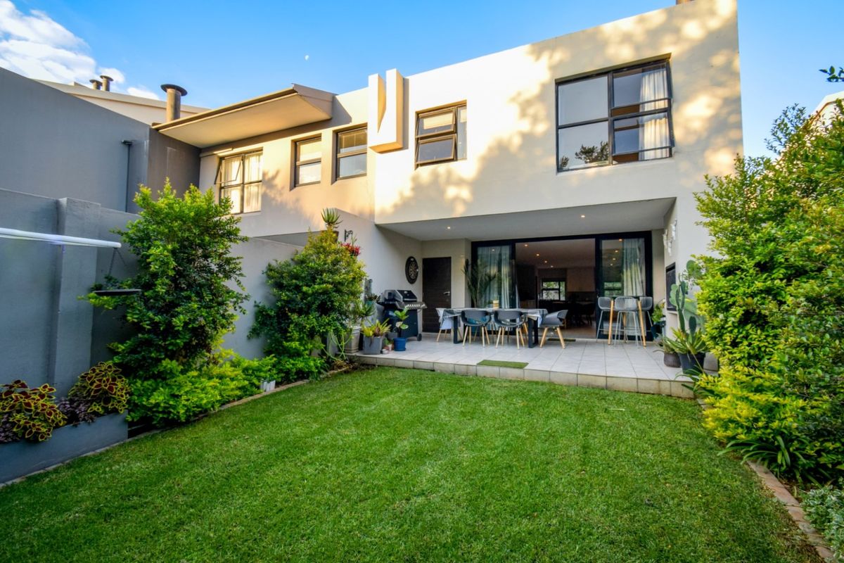 Rear view of the property featuring a paved patio area, built-in braai, and a well-maintained private garden with sliding door access to the interior.