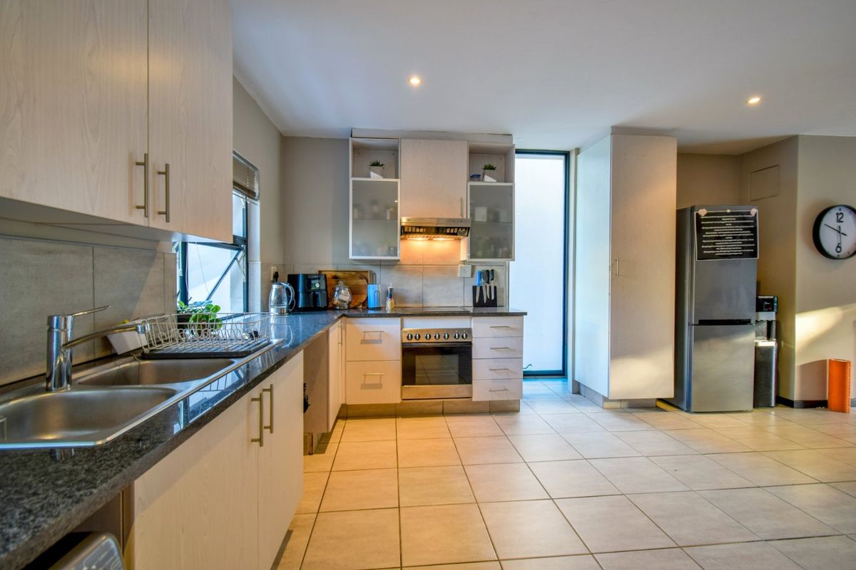 A functional kitchen featuring light wood cabinetry, granite countertops, stainless steel oven, extractor fan, and tiled flooring with ample natural light.
