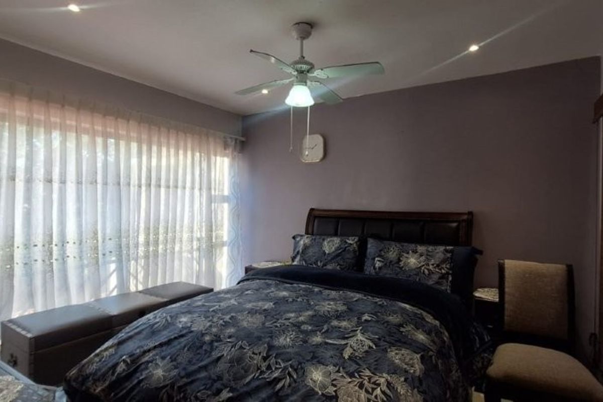A well-lit bedroom featuring a ceiling fan, recessed lighting, and a large window with sheer curtains, providing a comfortable and functional living space.