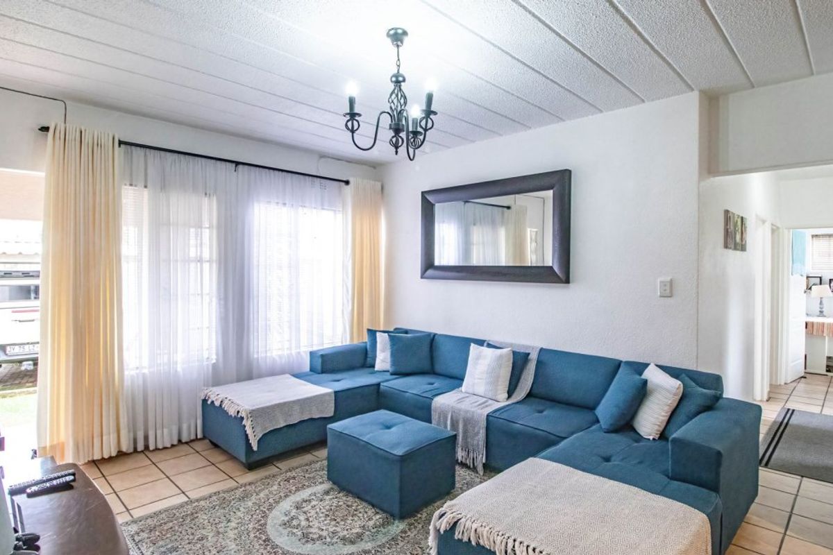 A bright living room featuring tiled flooring, a textured ceiling, and a decorative chandelier, with direct access to an outdoor area via a security gate.