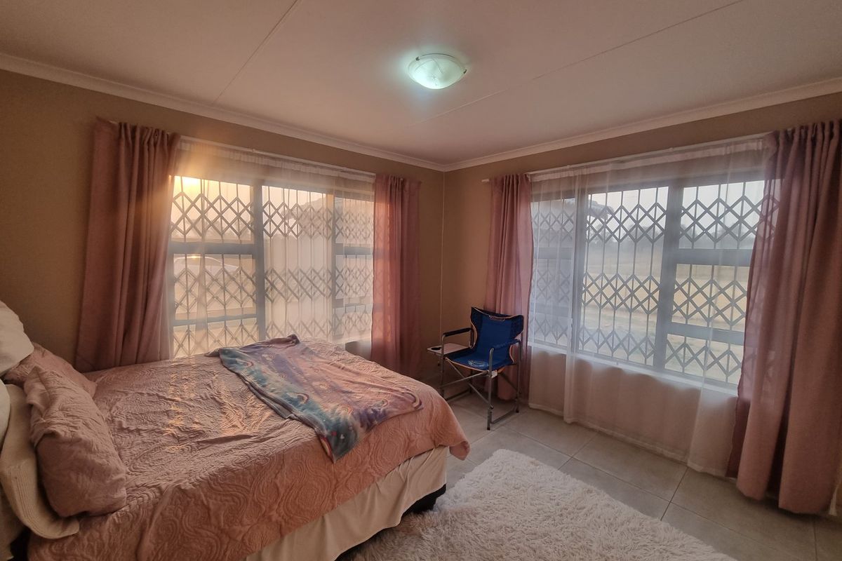 A bedroom featuring tiled flooring, large windows with fitted security gates, and neutral wall finishes.