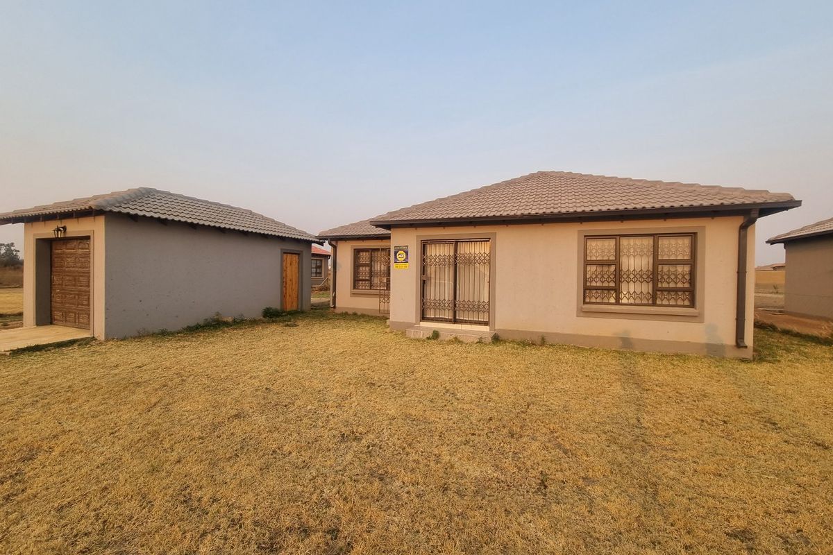 Rear view of a single-story house featuring a tiled roof, security gates, and a detached garage set on a large grassed plot.