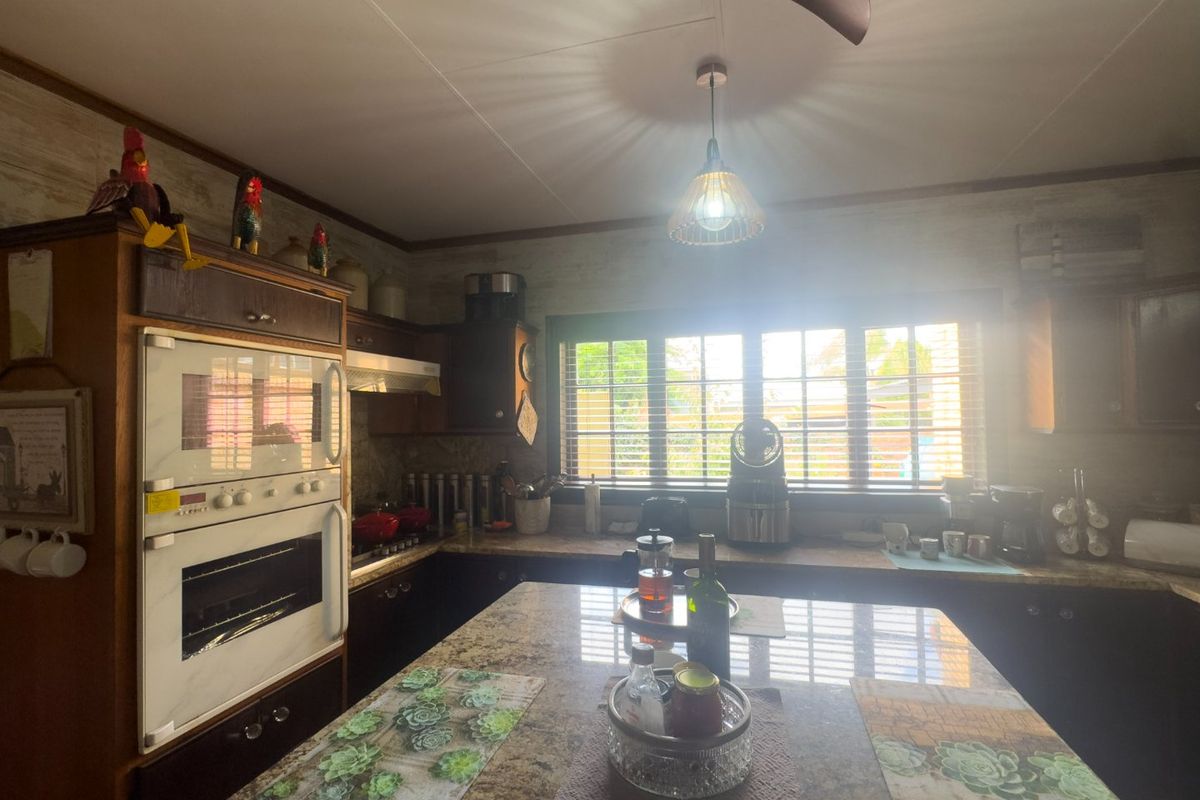 A functional kitchen featuring a central island, granite countertops, and a built-in double oven, illuminated by natural light through window blinds.