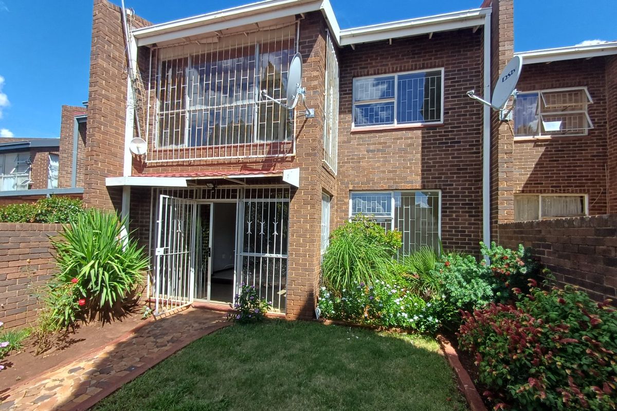 Rear view of a face brick townhouse featuring a small private garden, paved walkway, and security bars on windows and doors.