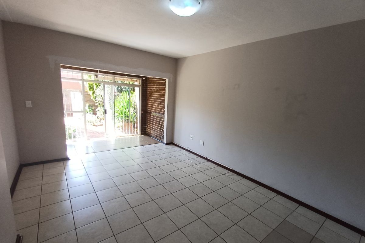 An empty living room featuring ceramic floor tiles, an exposed brick accent wall, and a sliding glass door providing access to the outdoor area.