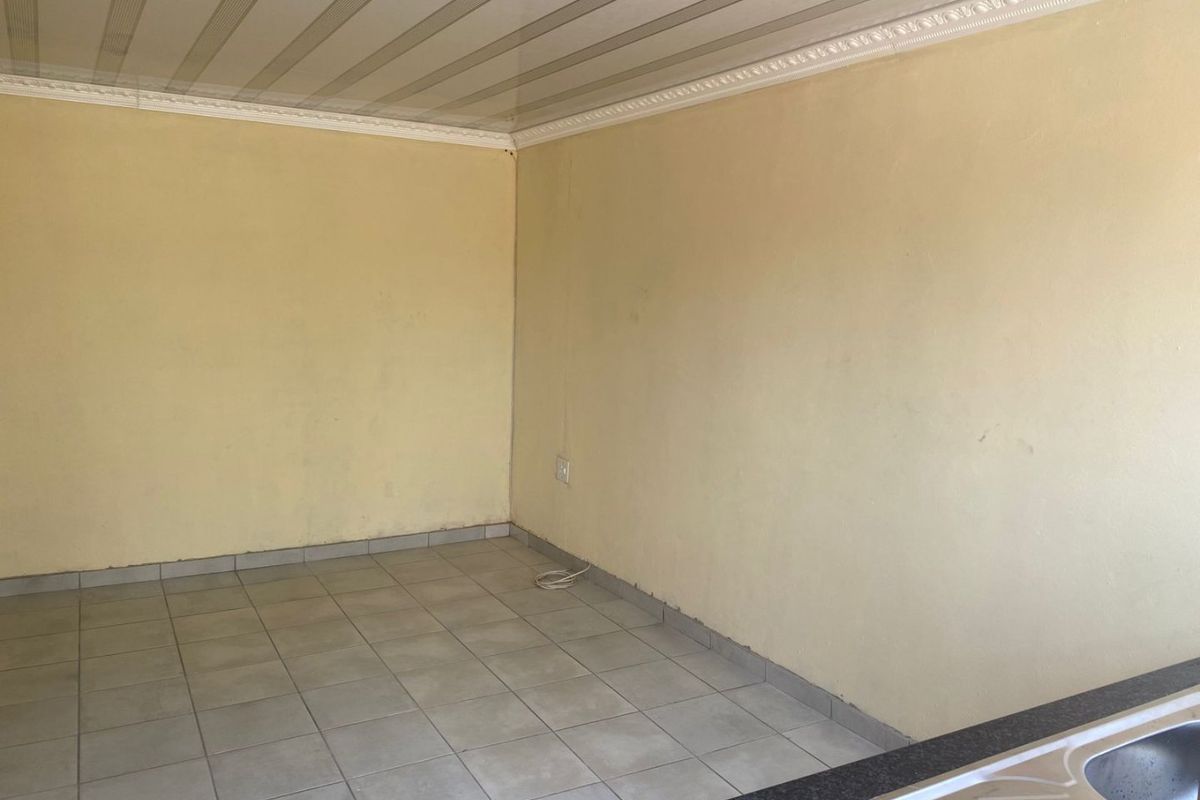 An empty kitchen area featuring tiled flooring, a sink with a laminate countertop, and decorative ceiling cornices, ready for renovation or personalization.