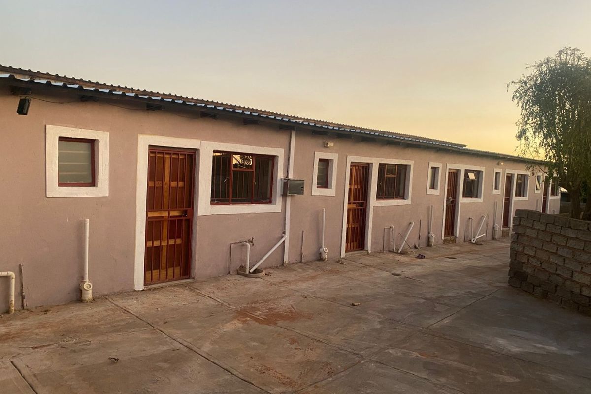 Rear exterior view of a multi-unit residential building featuring concrete paving, security gates, and exposed exterior plumbing infrastructure.