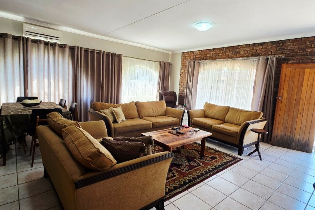 Spacious living area featuring ceramic floor tiles, an exposed brick feature wall, and a wall-mounted air conditioning unit.