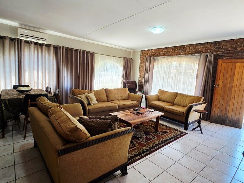 Spacious living area featuring ceramic floor tiles, an exposed brick feature wall, and a wall-mounted air conditioning unit.