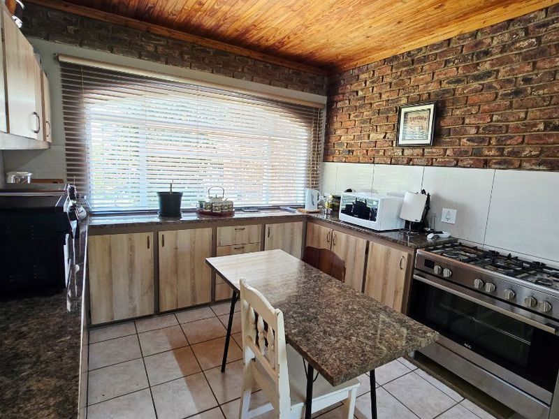 A functional kitchen featuring exposed brick walls, timber ceiling, granite countertops, and a gas stove with oven.