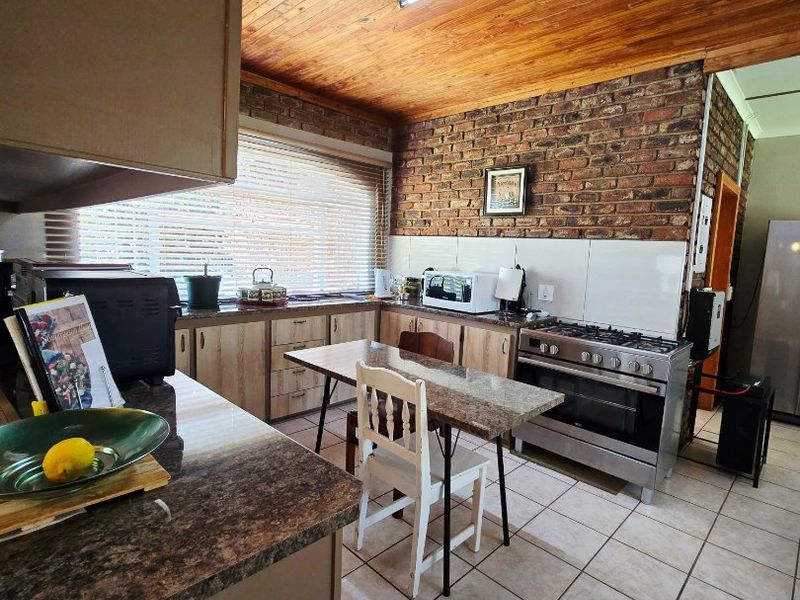 A rustic kitchen featuring exposed brick walls, a timber ceiling, tiled flooring, and a gas stove with ample counter space.