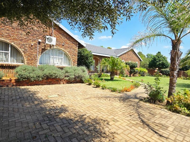 A well-maintained face brick house exterior featuring arched windows, a paved driveway, and a landscaped garden area.