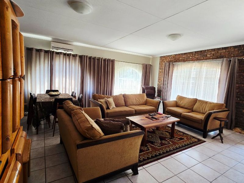 Spacious open-plan living and dining area featuring tiled floors, an exposed brick feature wall, and a wall-mounted air conditioning unit.