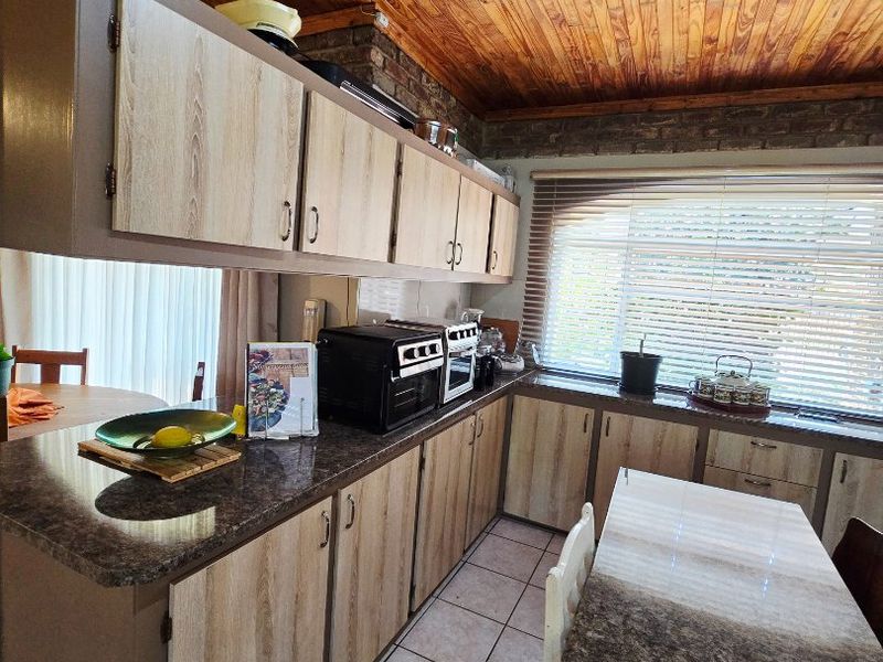 A functional kitchen featuring laminate cabinetry, granite countertops, tiled flooring, and a distinctive timber tongue and groove ceiling with exposed brick accents.
